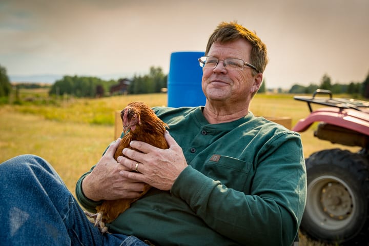 Andy of Purely By Chance Farm sitting in a chair holding one of his egg laying ladies.