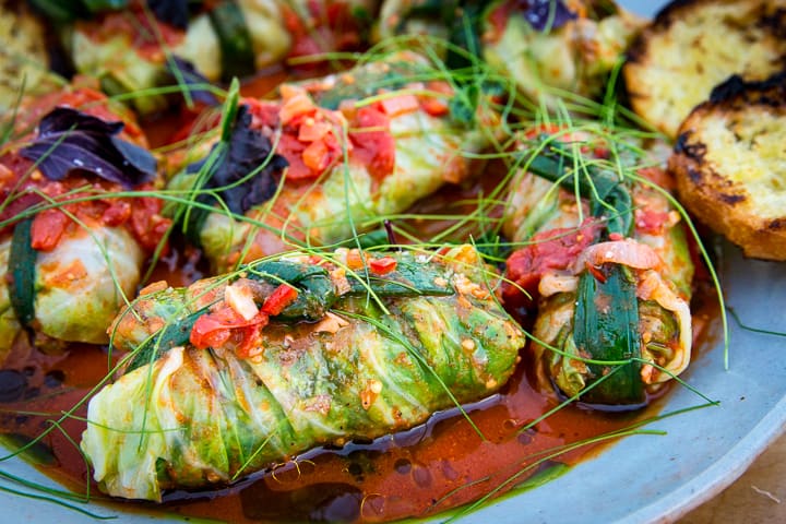 Chorizo Stuffed Cabbage with Carrot and Tomato Sauce in a braiser pan and topped with thin micro chives and hand torn basil