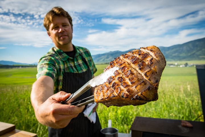 Chef Eric Wilson holds up a pork belly with the top fat cap scored in a cross hatch and perfectly charred. 