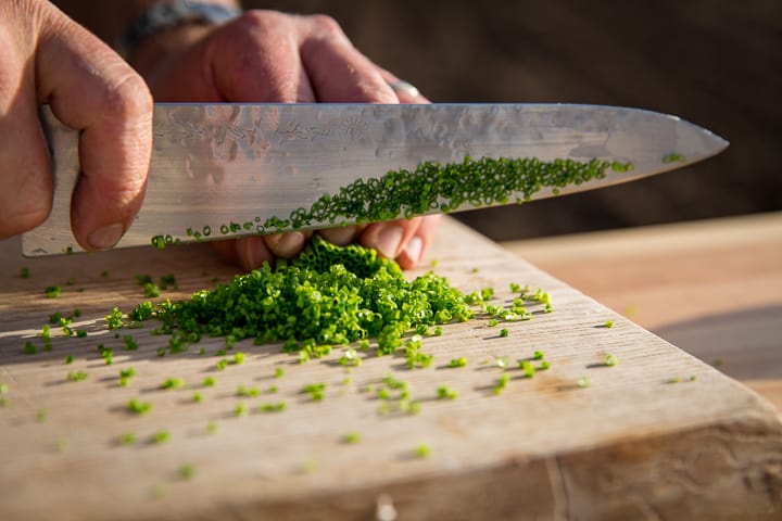 Chef Eric Wilson finely cutting chives to top the potato latkes and cast-iron potato gratin