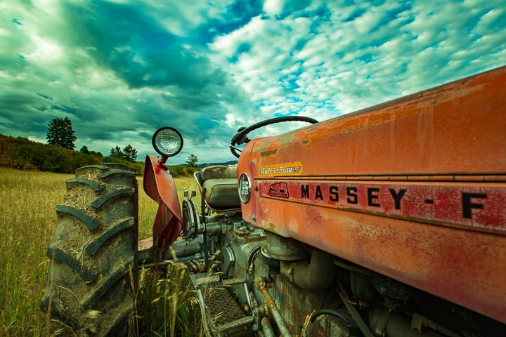 An old and beloved Massey farm tractor parked in a field on Teton Full Circle Farm. Dirt sticks to the wheels and the orange paint is showing years of use with a beautiful fading patina
