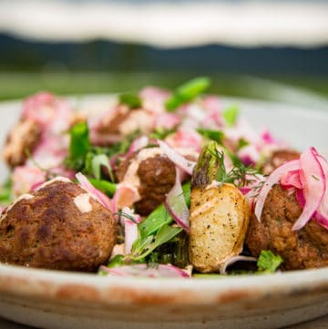 pan-roasted lamb meatballs plated with sautéed greens and turnips. Garnished with a tangy sumac yogurt sauce, pickled red onions, and a scattering of fresh herbs