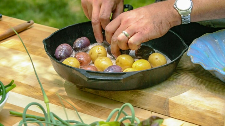 Two hands placing oiled potatoes on a bed of salt covering the bottom of a cast iron pan