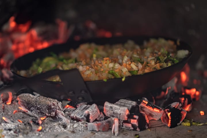 Steel pan sautéing Wood Fired Shaved Brussels Sprouts with mirepoix in a wood fire oven on a bed of coals