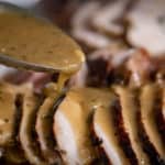 A spoon pouring the Wood Fired Turkey Gravy of sliced turkey