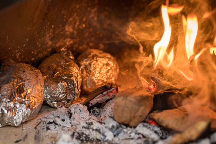 Roasting foil wrapped Wood Fired Brown Butter Yams in a wood fired oven next to a live fire