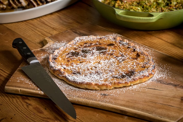 Wood Fired Pumpkin Crostata dusted with powdered sugar sitting on cutting board with a knife on the side ready to cut