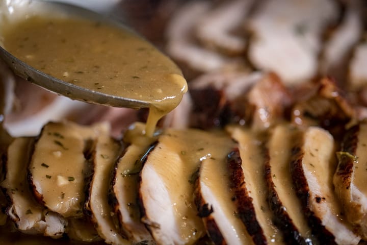 A spoon pouring the Wood Fired Turkey Gravy of sliced turkey