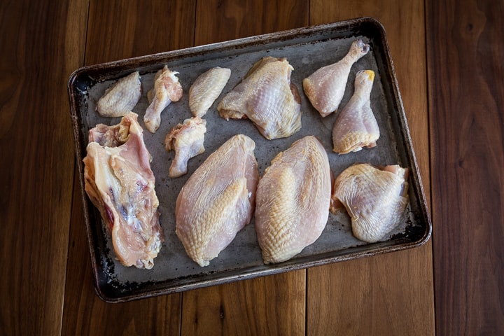 A whole chicken broken down into 10 pieces and the carcass laid out on a baking sheet