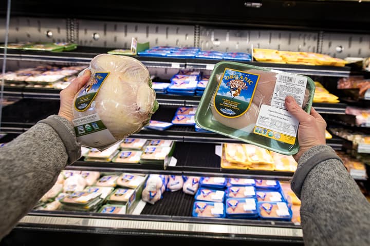 A shopper POV holding up both hands and comparing a whole chicken in one hand to individual breast pieces in the other