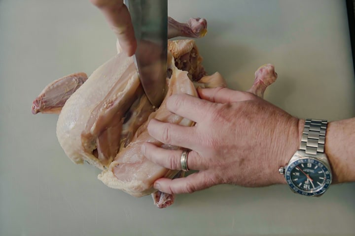 Breaking down a whole chicken. Cutting down along breastbone and ribs to remove chicken breast.