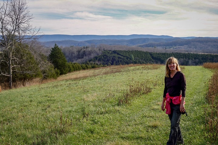 Erika standing in wide ope hill top with rolling hills beyond searching for farmland back East