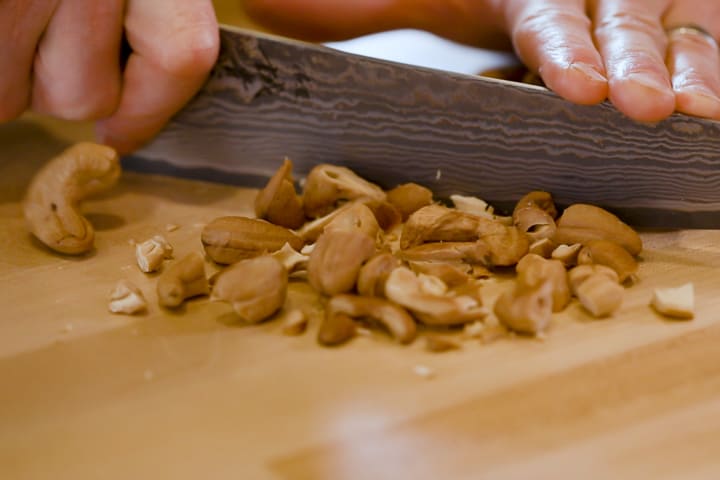 Close up on a knife rough chopping roasted cashews for Backcountry Curry Chicken Salad